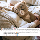 Percy bear with glasses and a stitched smile rests on a person's lap in a cozy knit sweater, with a social media comment overlay at the bottom.