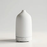A minimalist white diffuser with a textured matte finish and a sleek cylindrical base, shown against a clean light gray studio background.