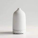 A minimalist white diffuser with a textured matte finish and a sleek cylindrical base, shown against a clean light gray studio background.