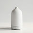 A minimalist white diffuser with a textured matte finish and a sleek cylindrical base, shown against a clean light gray studio background.