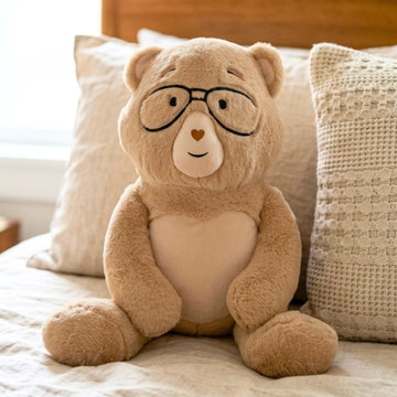 Percy bear with glasses on a bed with pillows
