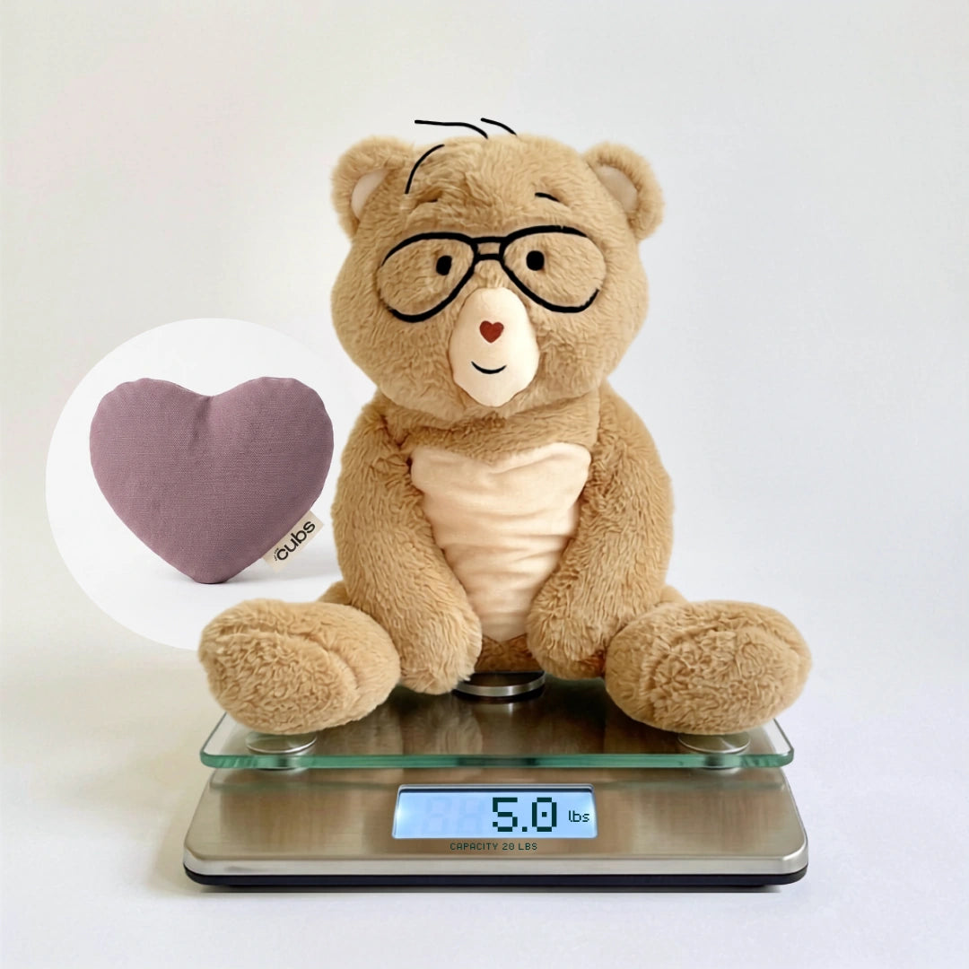 A beige plush teddy bear wearing black glasses sits on a digital scale, with a heart-shaped cushion shown in a circular inset. The scale displays 5.