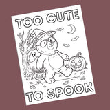 A black and white cartoon bear coloring page with Halloween illustrations, shown at an angle against a solid dark mauve background. The text reads 'TOO CUTE TO SPOOK'.