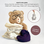 A teddy bear comfort bear wearing glasses, wrapped in a cream bag, with a dark purple heart-shaped pouch beside it. Text at the top lists included items: the bear, a thermal heart pouch, a wash bag, and free gift bag charms.